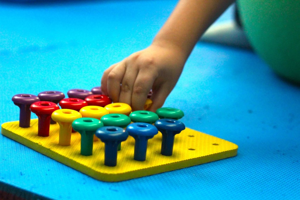 Niño realizando actividad de integración sensorial sobre pelota terapéutica clasificando objetos por color.