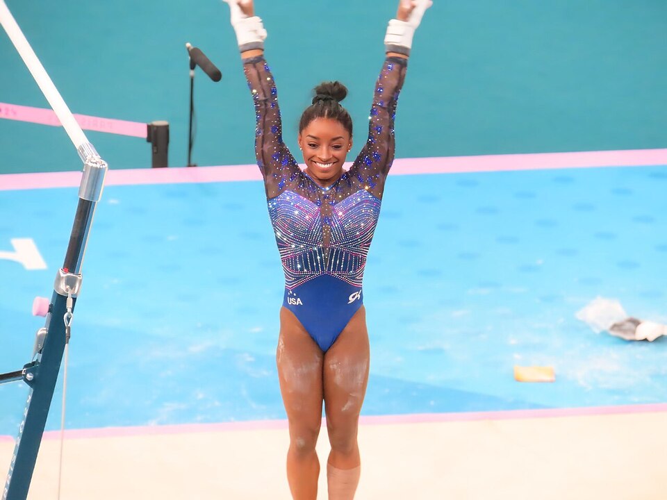 Simone Biles en pleno salto durante una competencia internacional de gimnasia artística, mostrando fuerza y concentración.