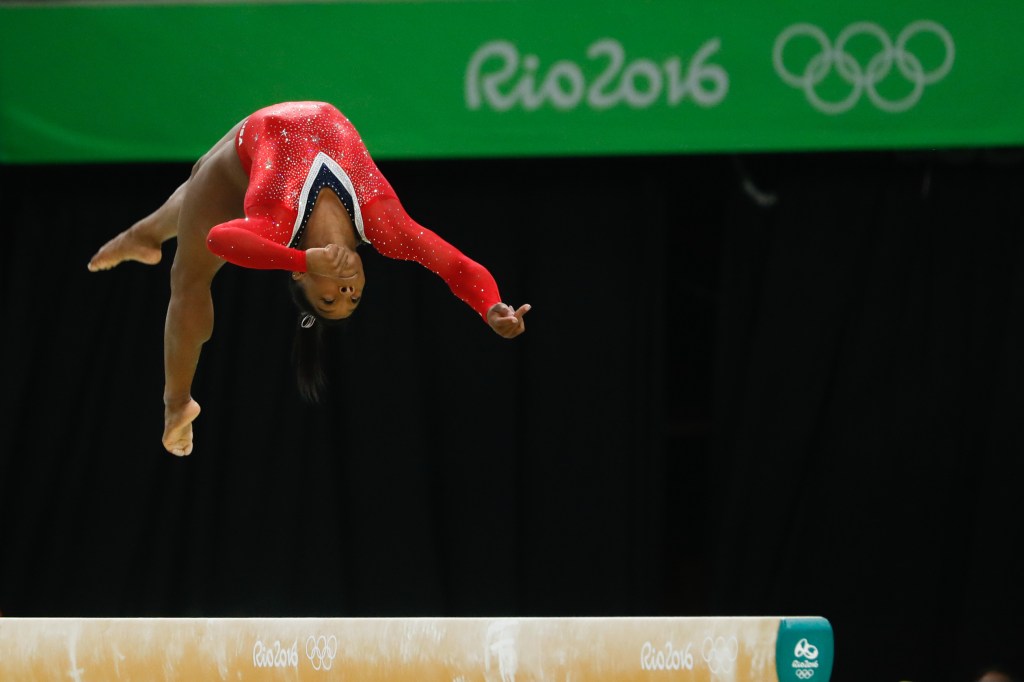 Simone Biles en pleno salto durante una competencia internacional de gimnasia artística, mostrando fuerza y concentración.